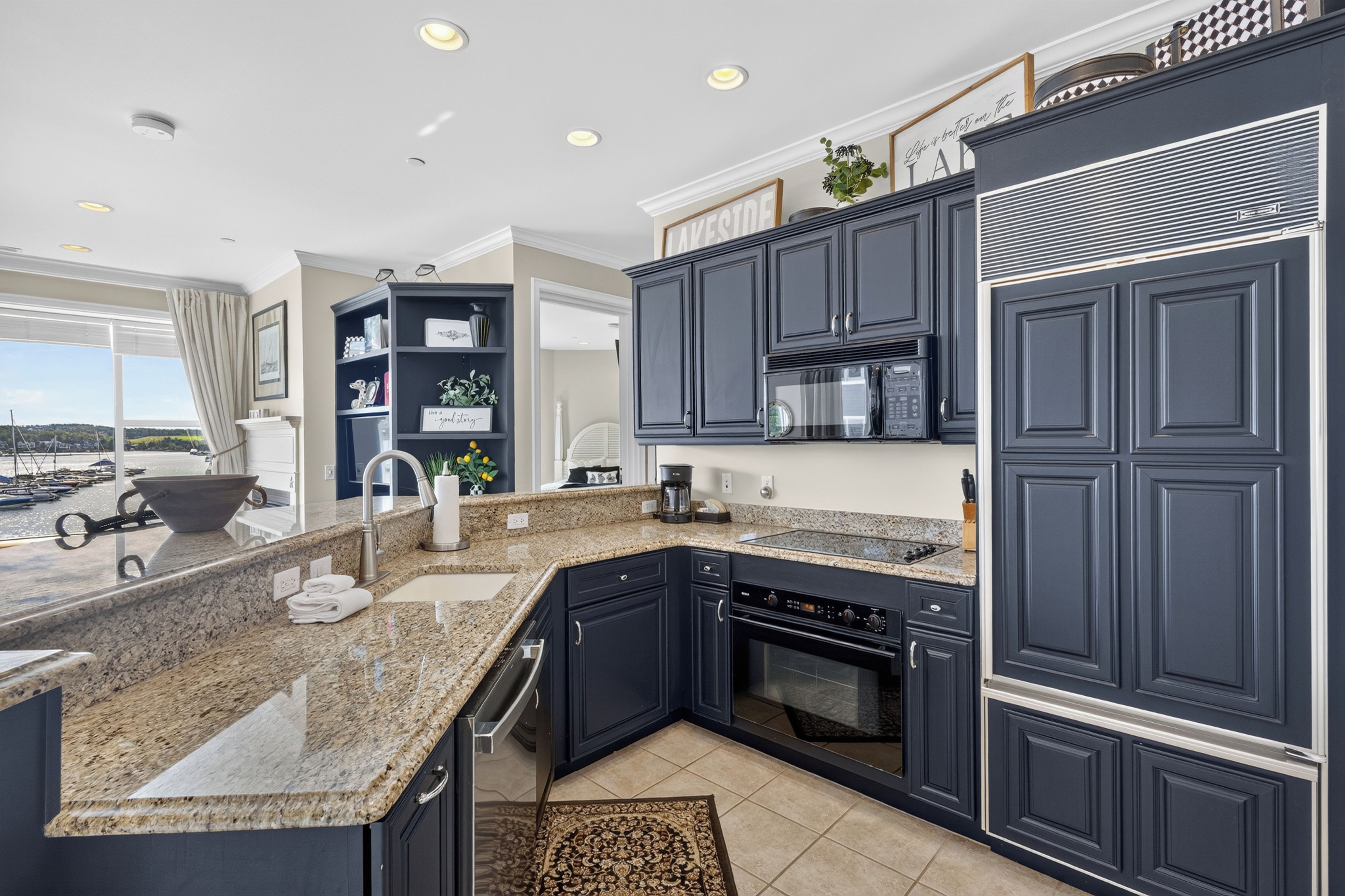 A modern kitchen with dark cabinetry, granite countertops, a built-in oven, and a coffee maker.