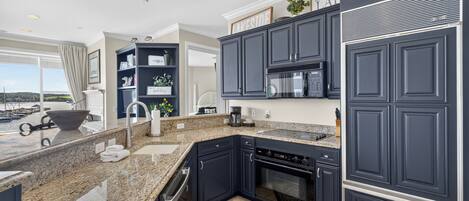 A modern kitchen with dark cabinetry, granite countertops, a built-in oven, and a coffee maker.