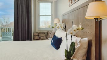 A hotel room with a large bed, a window with blinds, a lamp, and a potted orchid plant.