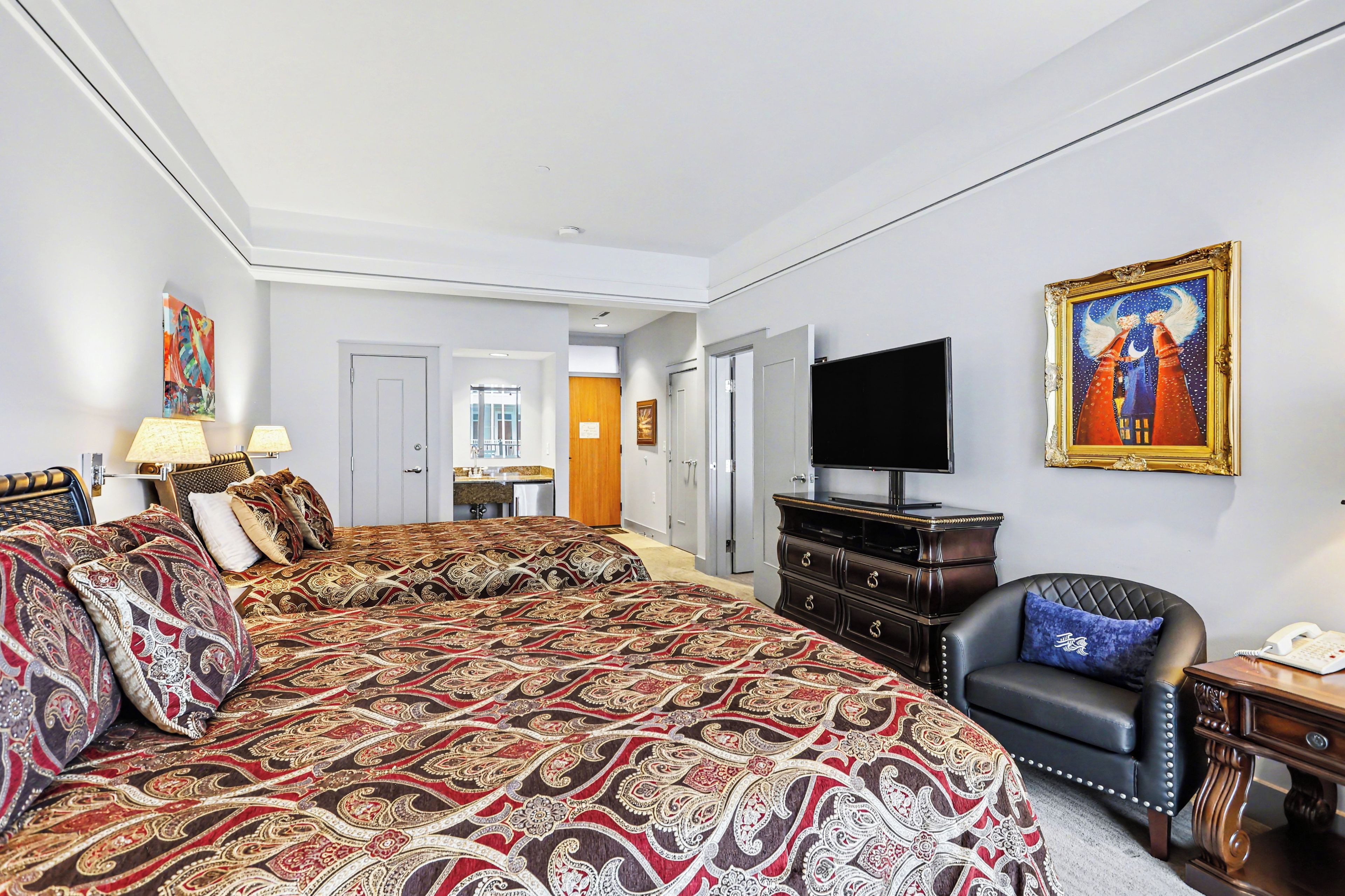 A hotel room with a large bed, a TV, a chair, and a dresser.