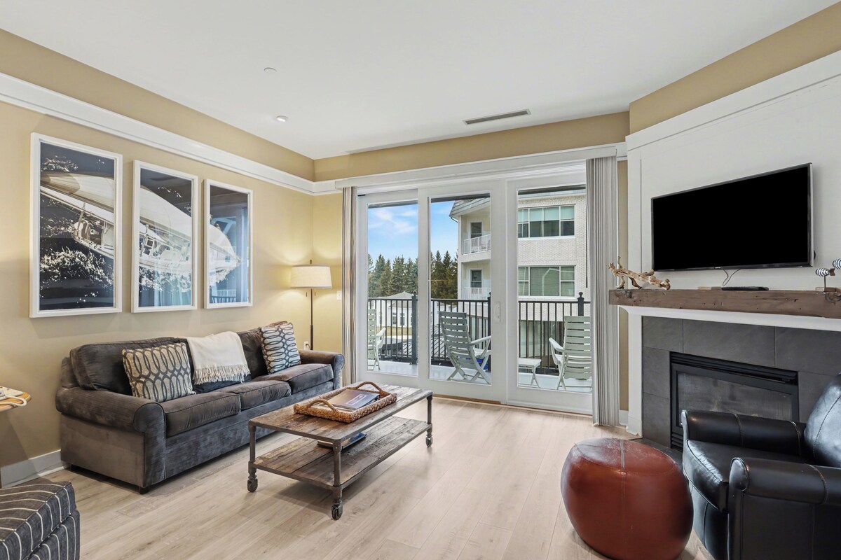 A living room with a sofa, coffee table, ottoman, and a fireplace.