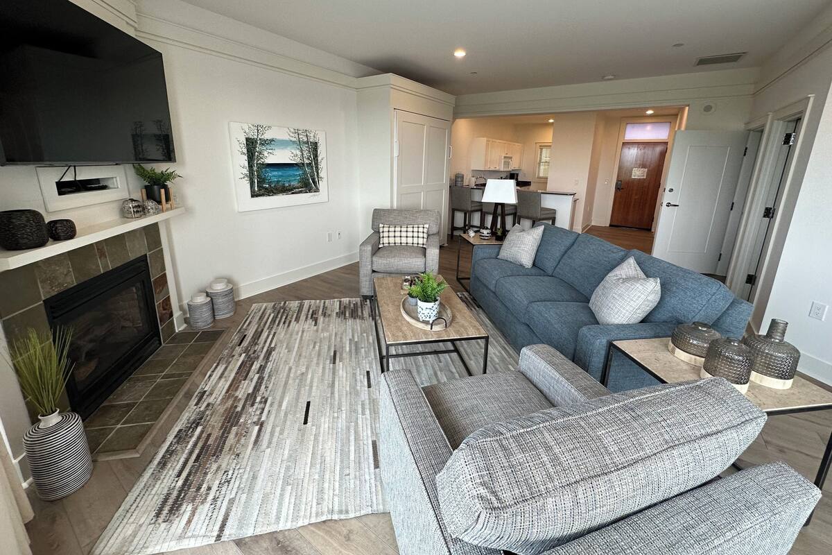 A modern living room with a fireplace, a grey sofa, a coffee table, and a flat-screen TV mounted above the fireplace.