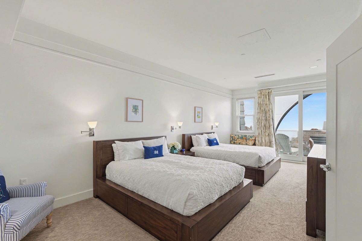 A hotel room with two beds, a sofa, a desk, and a view of the sky.