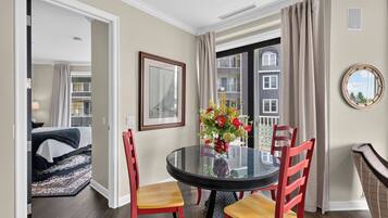A dining area with a glass table, red chairs, a vase of flowers, a framed picture, and a view of a building through a window.