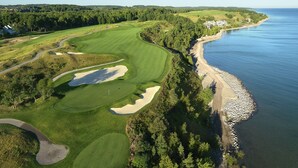 An aerial view of a golf course with sand bunkers, a water body, and a forested area. - Village Suites Bay Harbor (Petoskey)