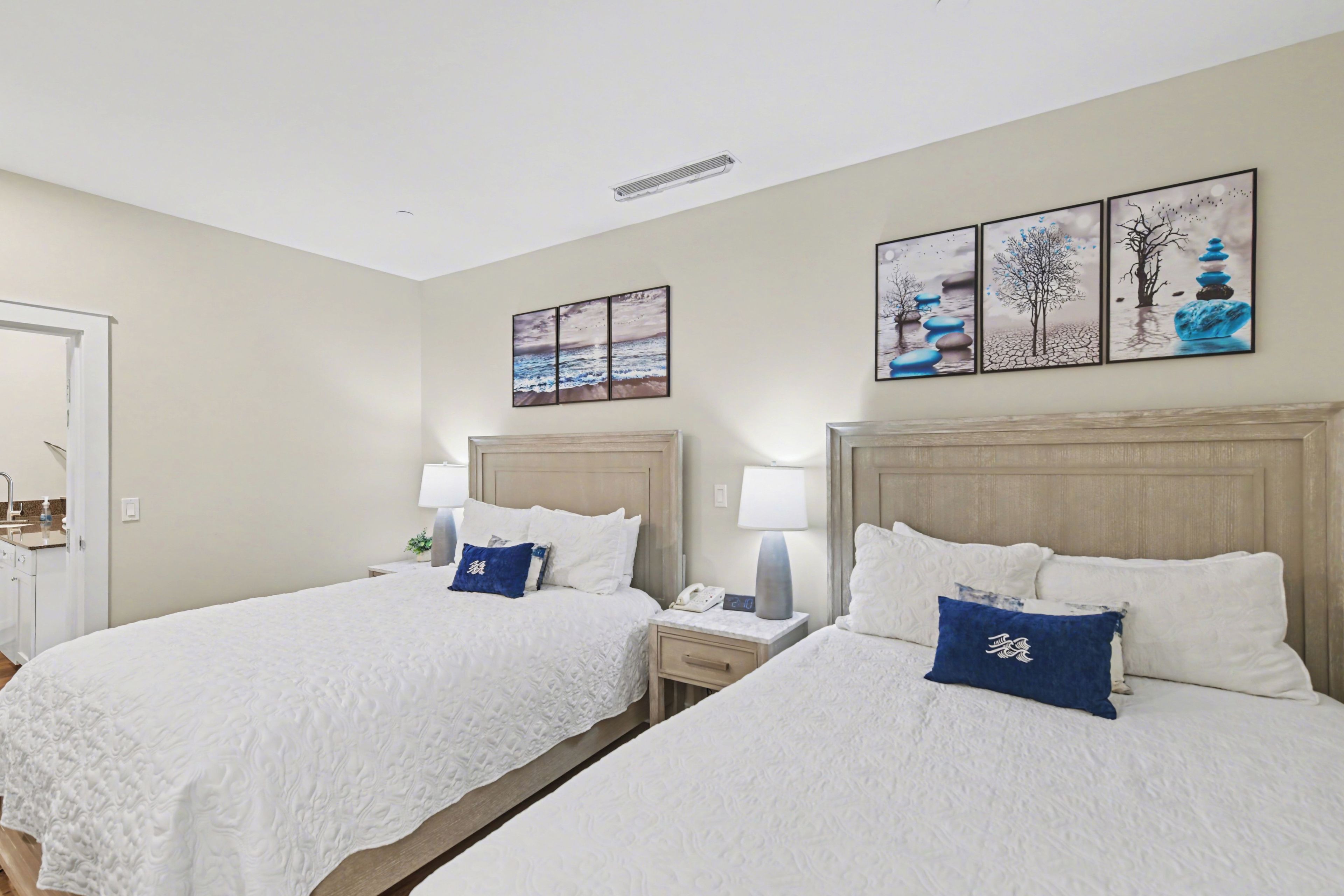 A hotel room with two beds, bedside tables, lamps, and artwork on the wall.