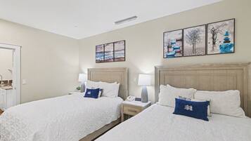 A hotel room with two beds, bedside tables, lamps, and artwork on the wall.