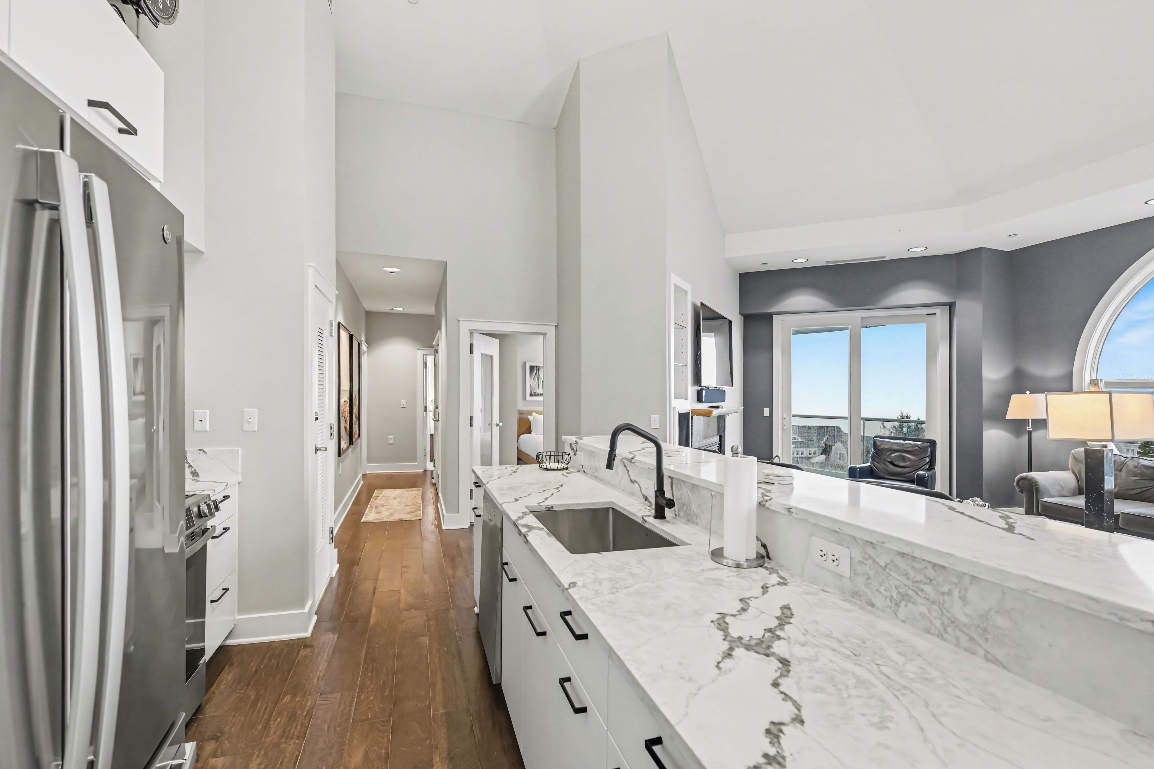 A modern kitchen with a marble countertop, stainless steel appliances, and a large window offering a view.