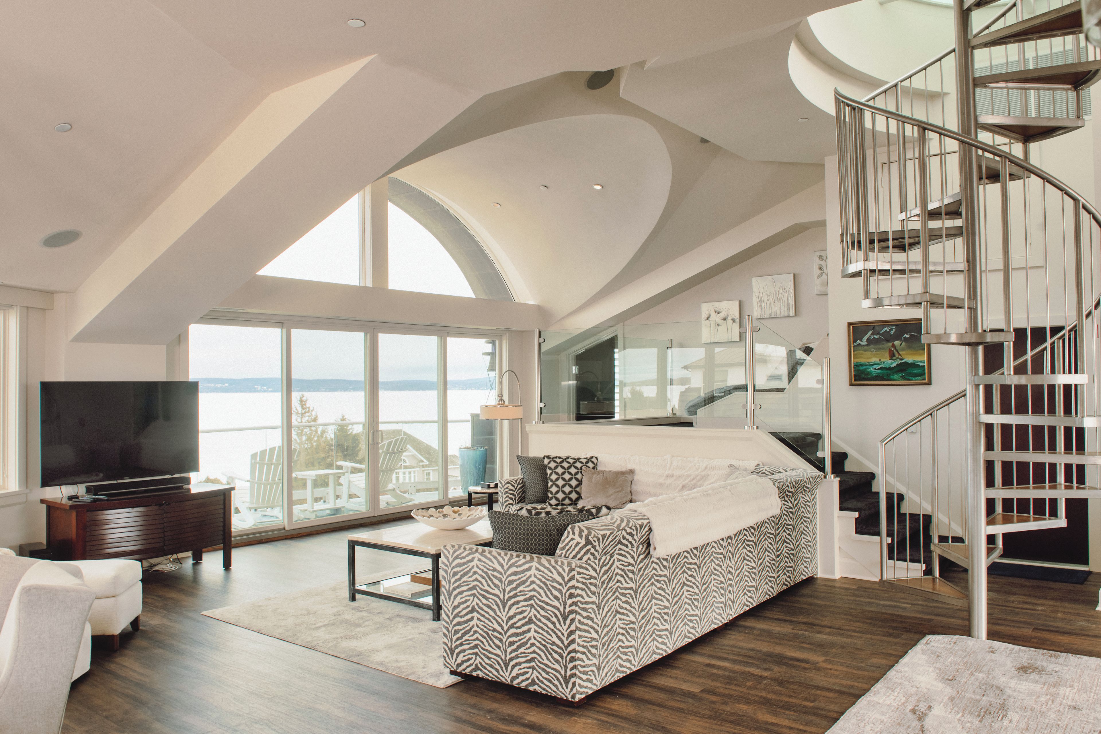 A spacious living room with a large window, a staircase, and a television.