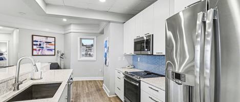 A modern kitchen with stainless steel appliances, a marble countertop, and a view to the outside.