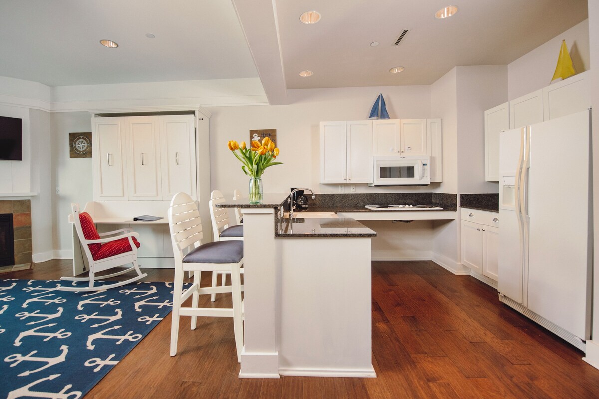 A modern kitchen with white cabinetry, a central island, a microwave, and a dining area with two chairs.