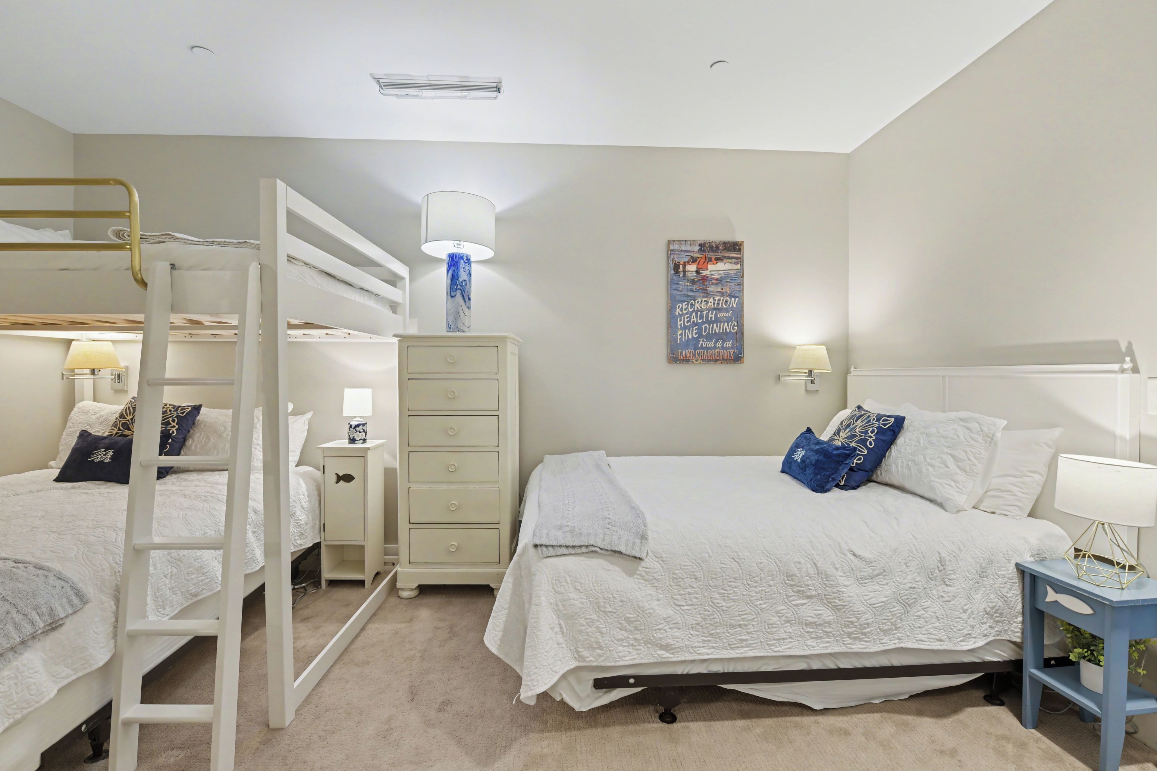 A bedroom with bunk beds, a dresser, bedside tables with lamps, and a poster on the wall.