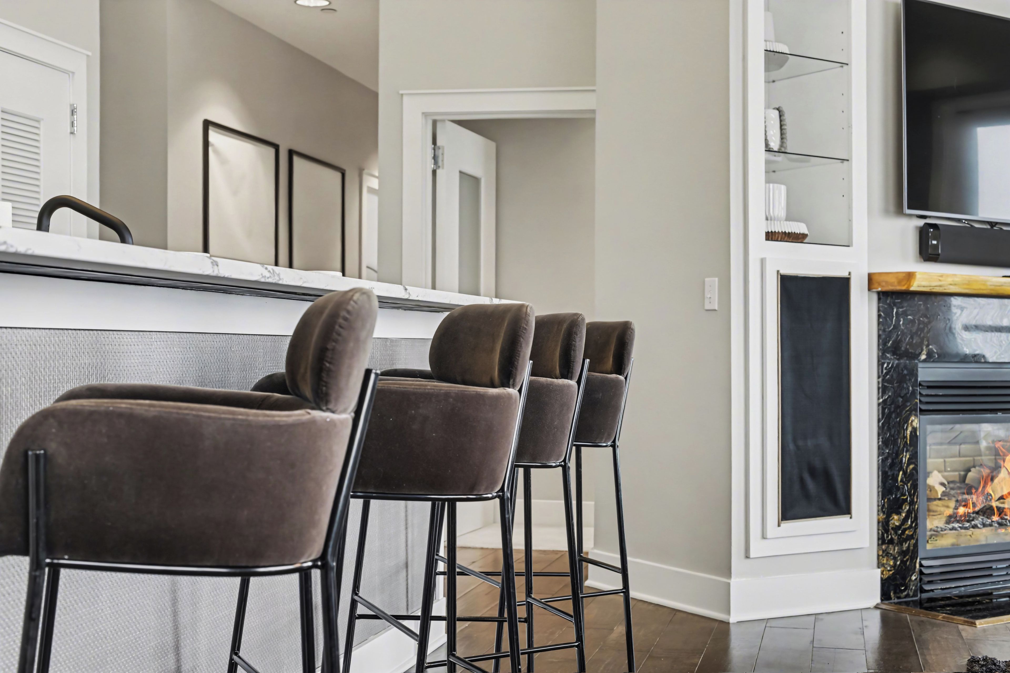 A kitchen with a marble countertop, a black TV mounted on the wall, and a fireplace with a glass front.