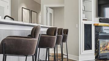 A kitchen with a marble countertop, a black TV mounted on the wall, and a fireplace with a glass front.