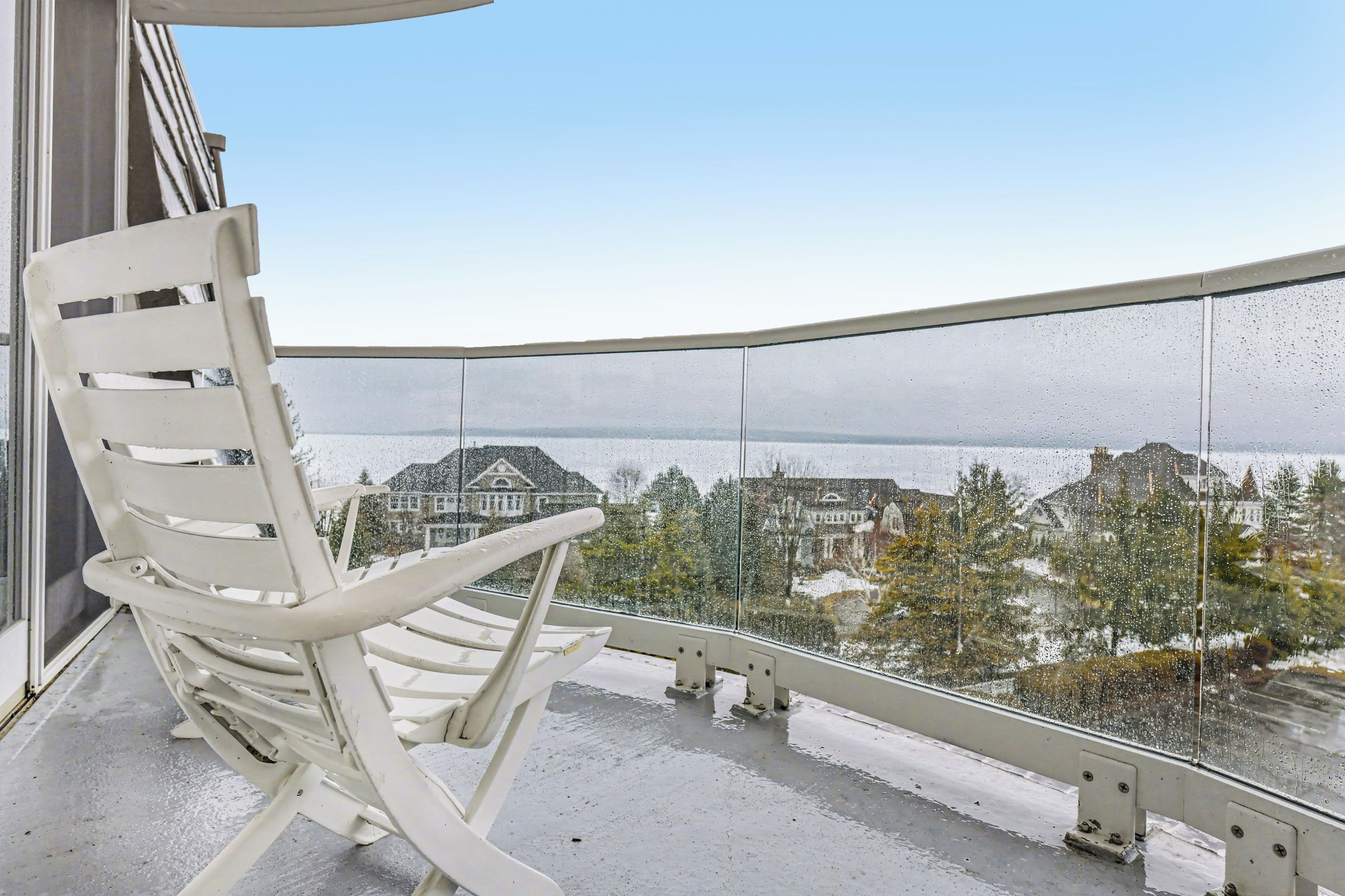 A white chair on a balcony with a view of a body of water and buildings.