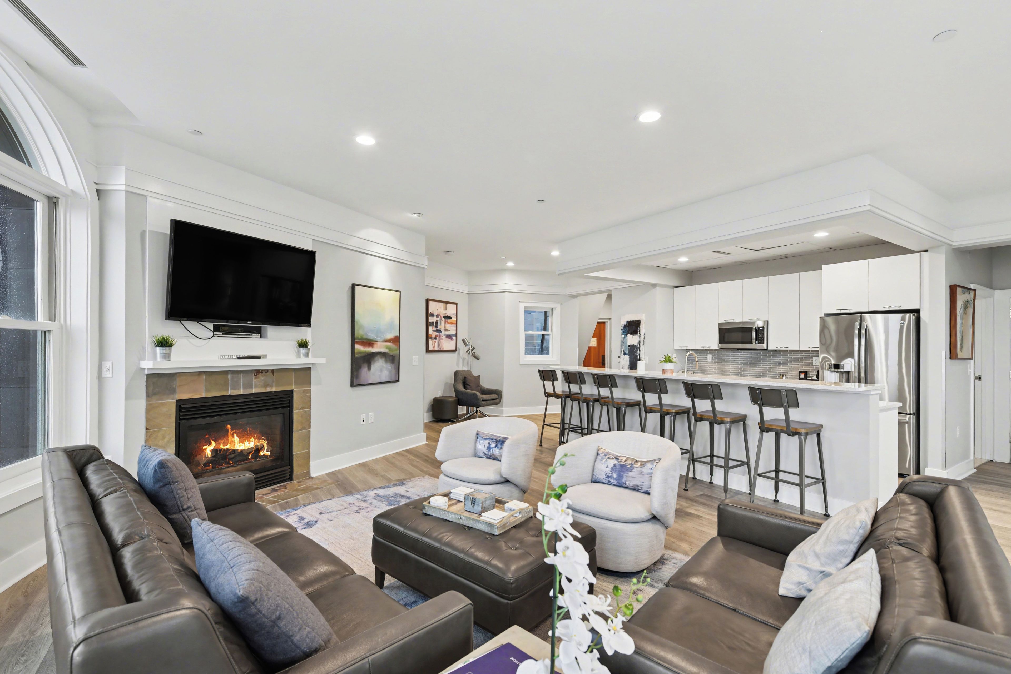 A modern living room with a fireplace, leather sofas, and a kitchen area with bar stools.