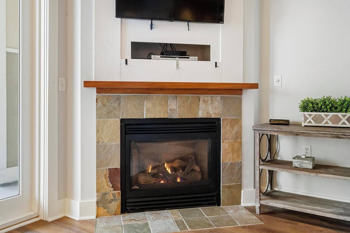 A fireplace with a stone surround, a mounted television above it, and a small shelf with decorative items.