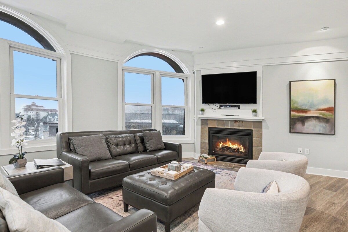 A living room with a fireplace, a sofa, a television, and large windows.