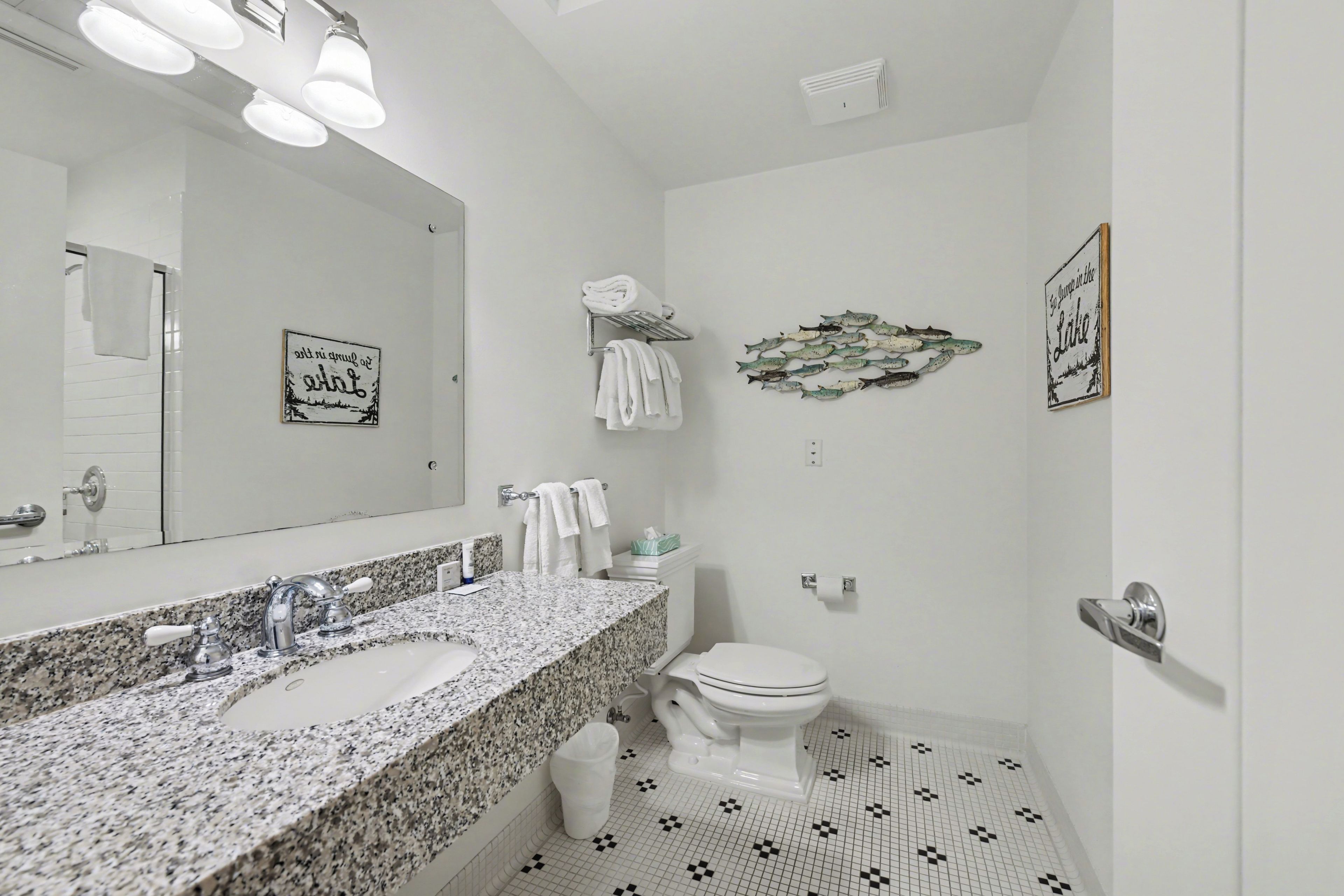 A bathroom with a granite countertop sink, a white toilet, and a wall-mounted towel rack.