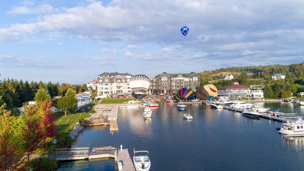 A marina with boats docked, a hot air balloon, and a large building with multiple stories. - Village Suites Bay Harbor (Petoskey)