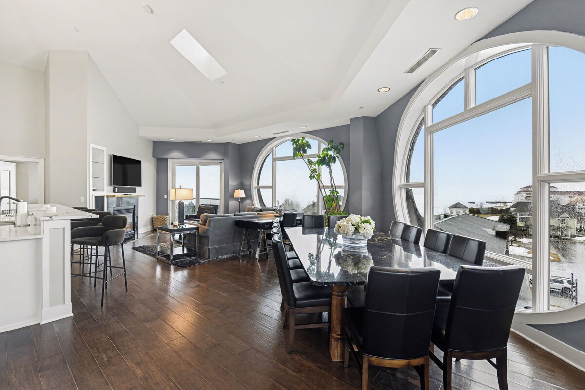 A modern kitchen with a large island, a dining area with a glass table, and large windows offering a view.