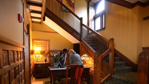 A staircase with a wooden handrail and patterned carpet, leading to a room with a wooden desk and a vase of flowers.