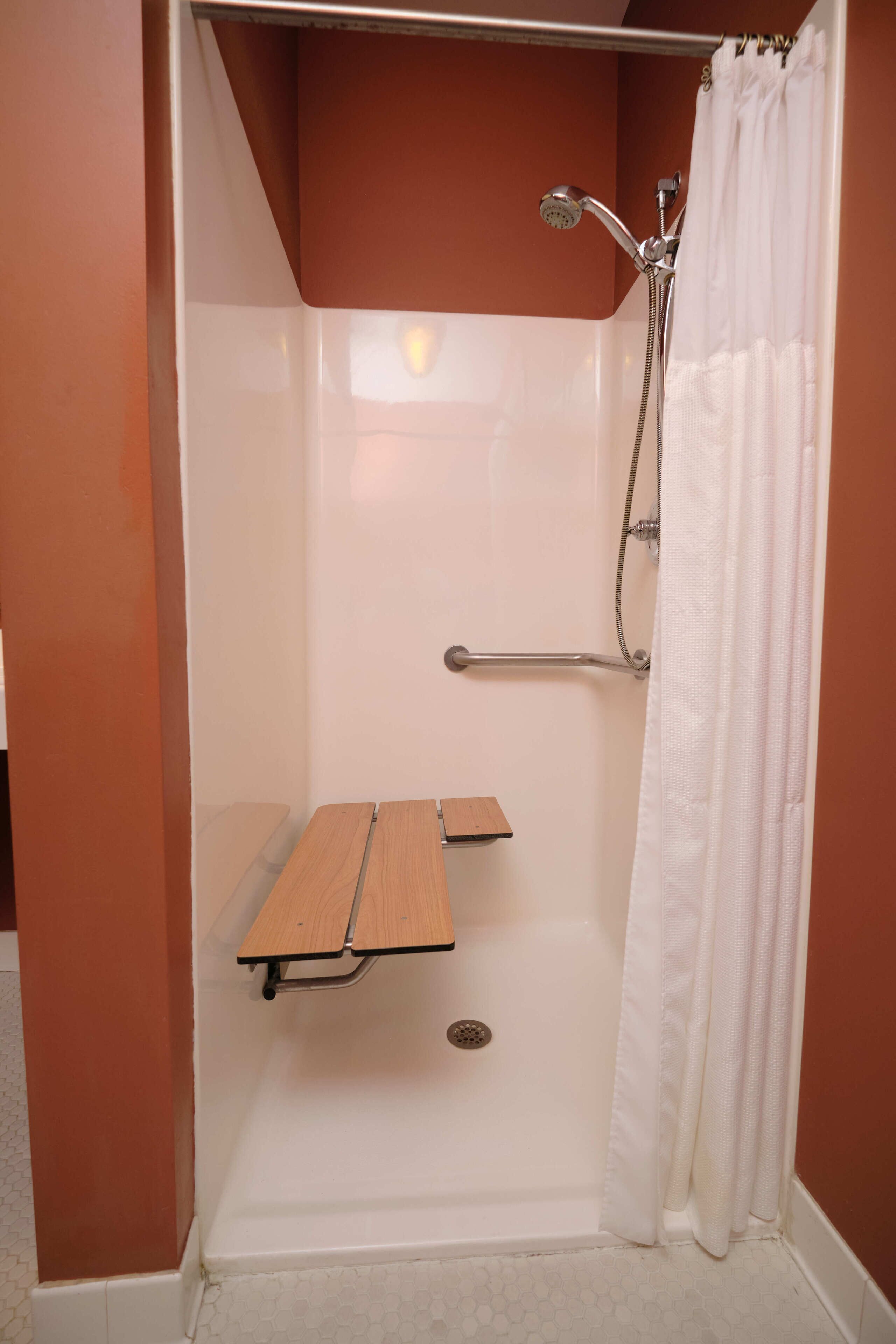 Une cabine de douche avec un rideau de douche blanc, une douchette à main et une barre d’appui.