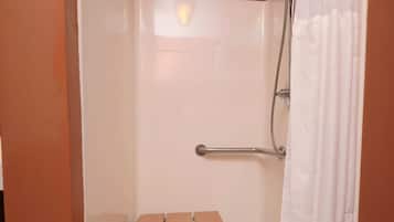 Une cabine de douche avec un rideau de douche blanc, une douchette à main et une barre d’appui.