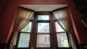 A bay window with curtains, a cushioned bench, and a view of a house through the window. - The Inn on Ferry Street (Detroit)