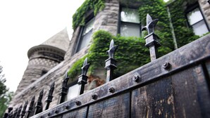 A stone building with ivy-covered walls and a wooden fence with pointed tops. - The Inn on Ferry Street (Detroit)