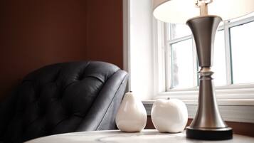 A table with a lamp and two white vases, a black leather chair, and a window with blinds.