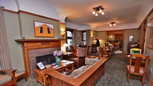 A spacious living room with a fireplace, wooden furniture, patterned carpet, and a dining area with chairs and a table. - The Inn on Ferry Street (Detroit)