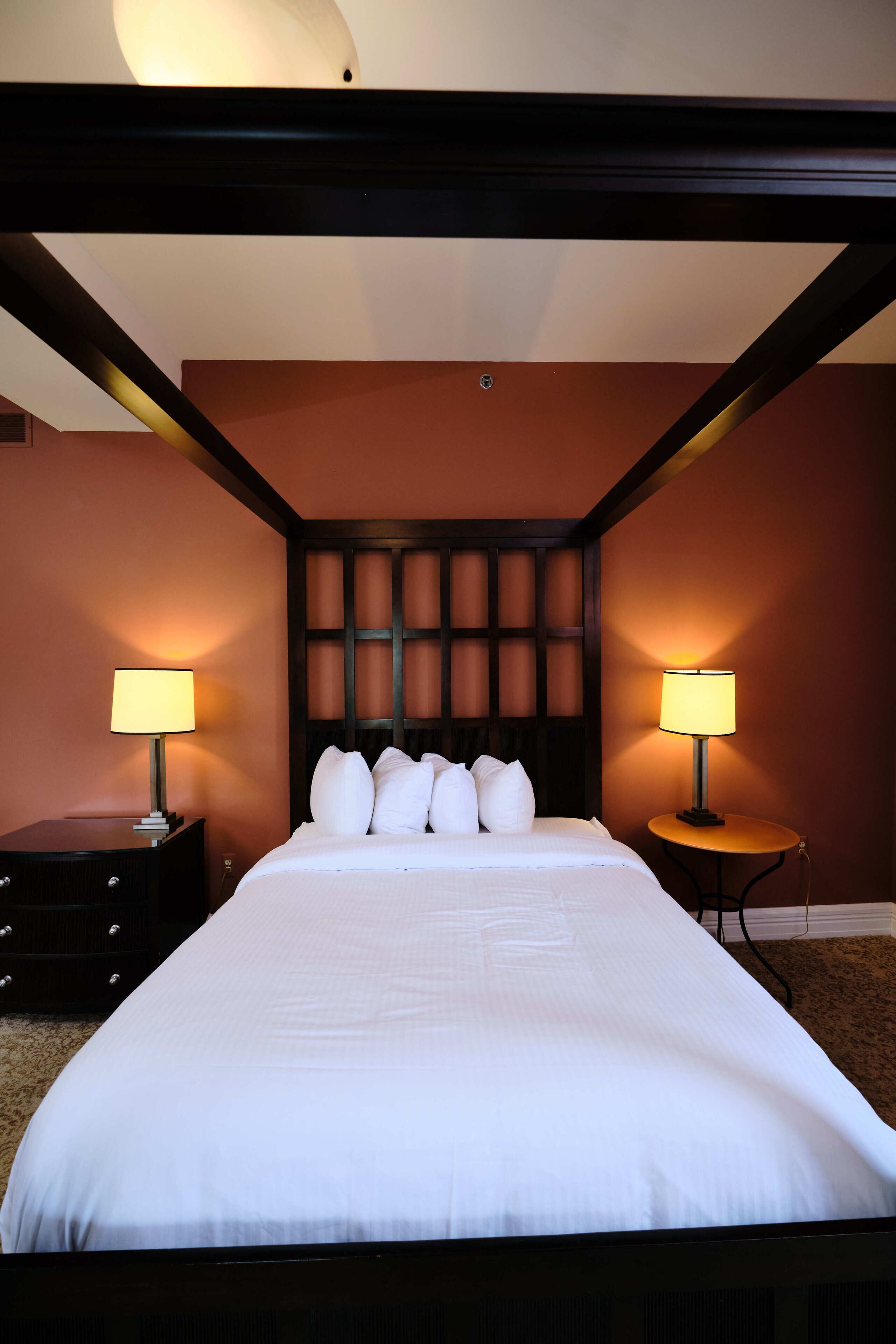 Une chambre d’hôtel avec un grand lit, deux tables de chevet avec des lampes et une tête de lit sombre.