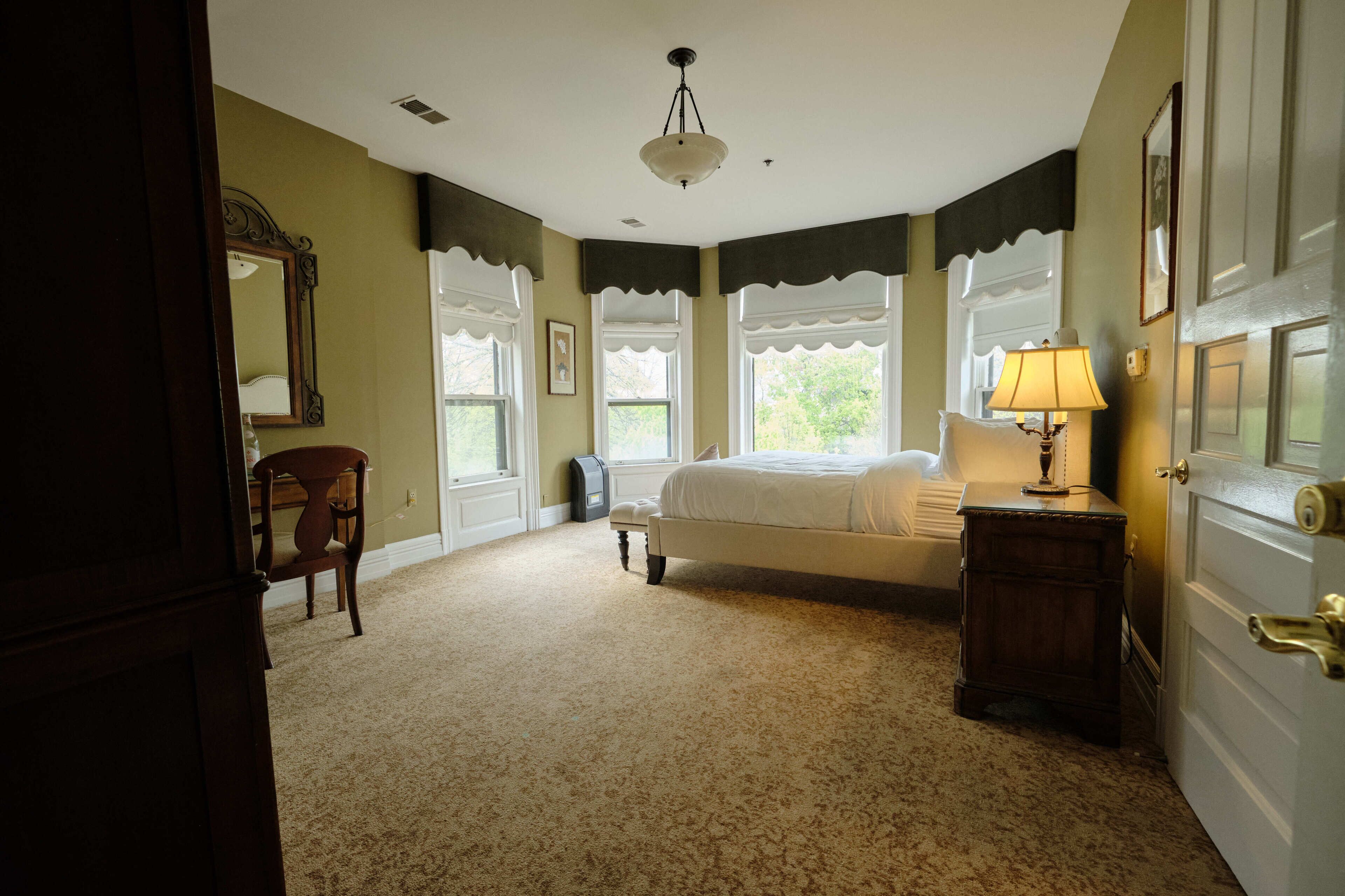 A bedroom with a bed, a chair, a nightstand, a lamp, and a door.
