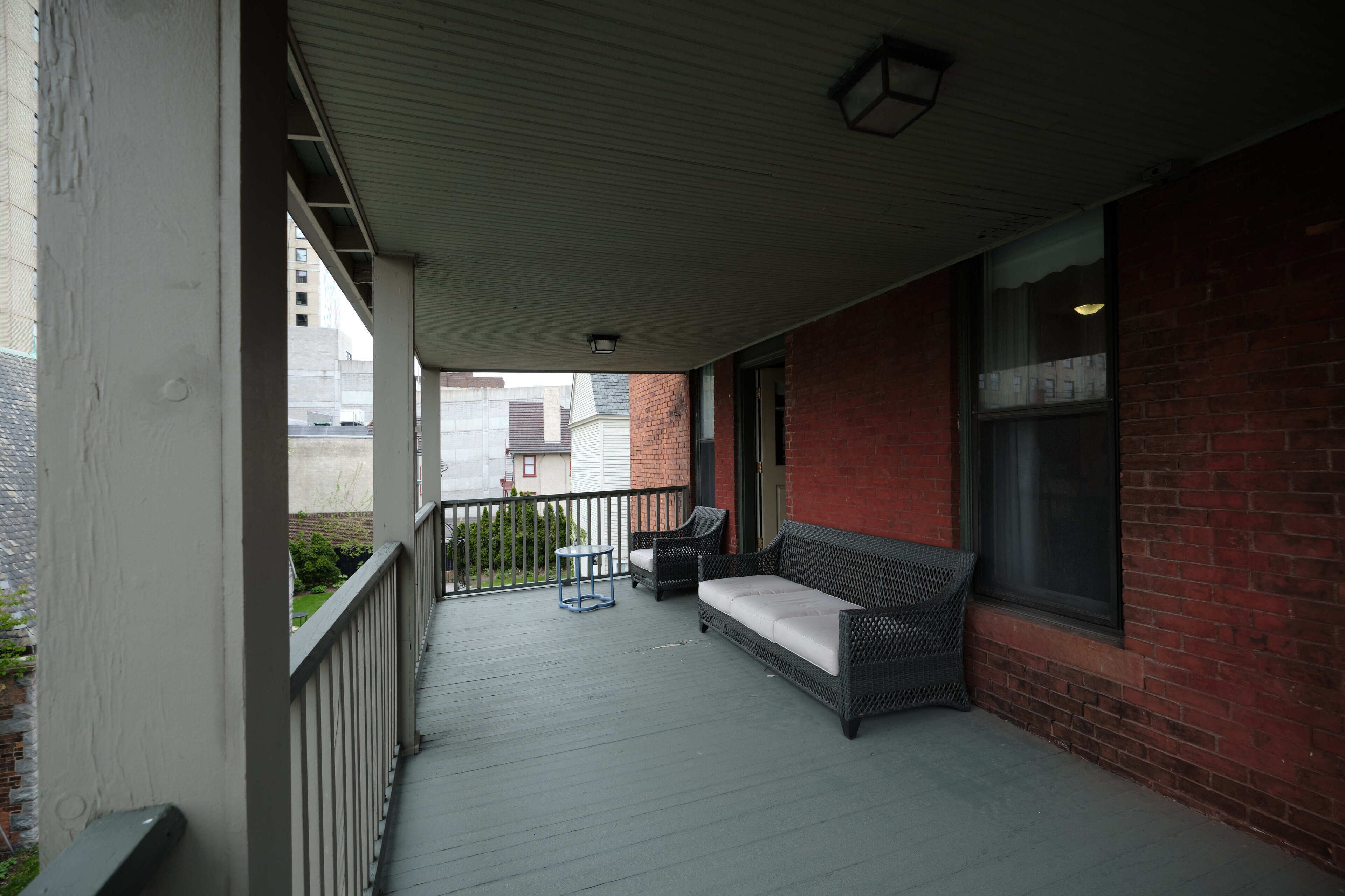 A covered porch with a wicker sofa and two chairs, a small table, and a window with a view of the street.