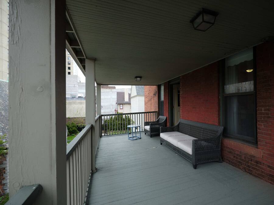 A covered porch with a wicker sofa and two chairs, a small table, and a window with a view of the street.