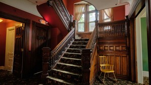 A grand staircase with ornate woodwork and a wooden chair at the bottom. - The Inn on Ferry Street (Detroit)