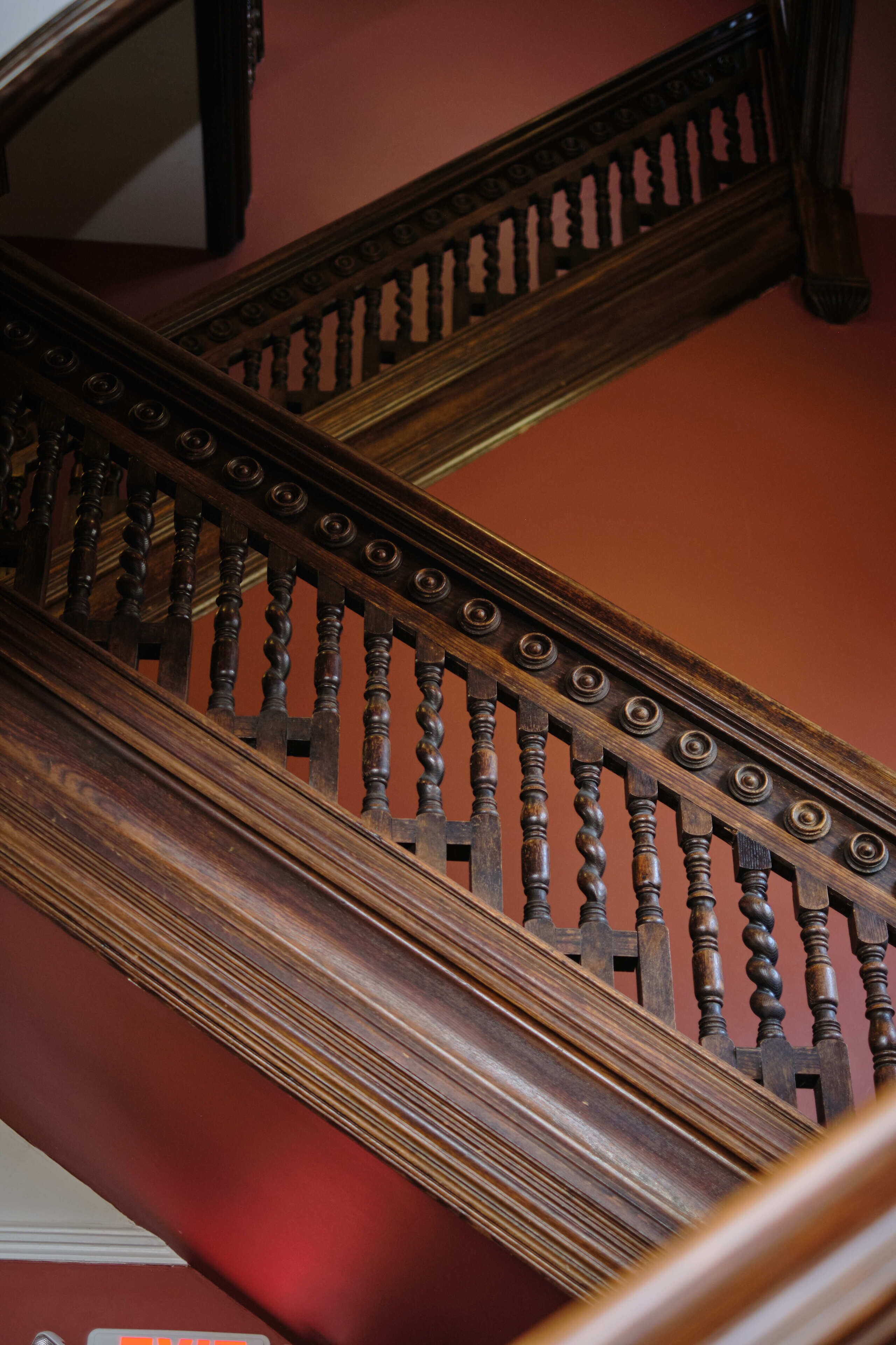 A wooden staircase with ornate balusters and a handrail, leading to an upper floor.