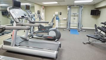 Un gimnasio con máquinas de cardio, equipo de levantamiento de pesas y un espejo grande.
