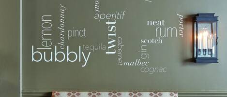 A wall with a word cloud of alcohol types, a table with a patterned tablecloth, and a lit candle on the table.