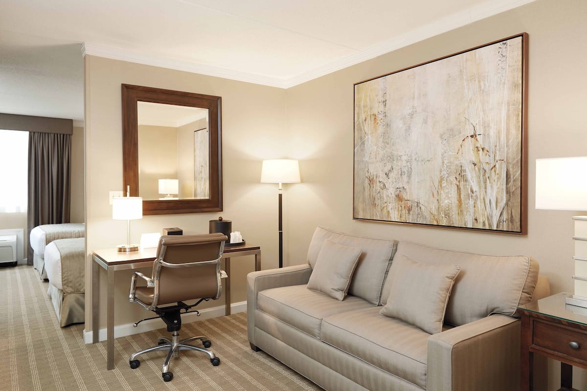 A hotel room with a bed, a desk with a chair, a sofa, a large abstract painting, and a lamp.