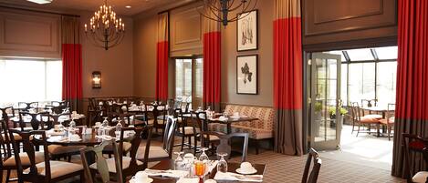 A large dining area with multiple tables set for service, a chandelier, and red curtains.