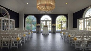 A wedding ceremony setup with white chairs, a central aisle, and a chandelier. - Ethan Allen Hotel (Danbury)