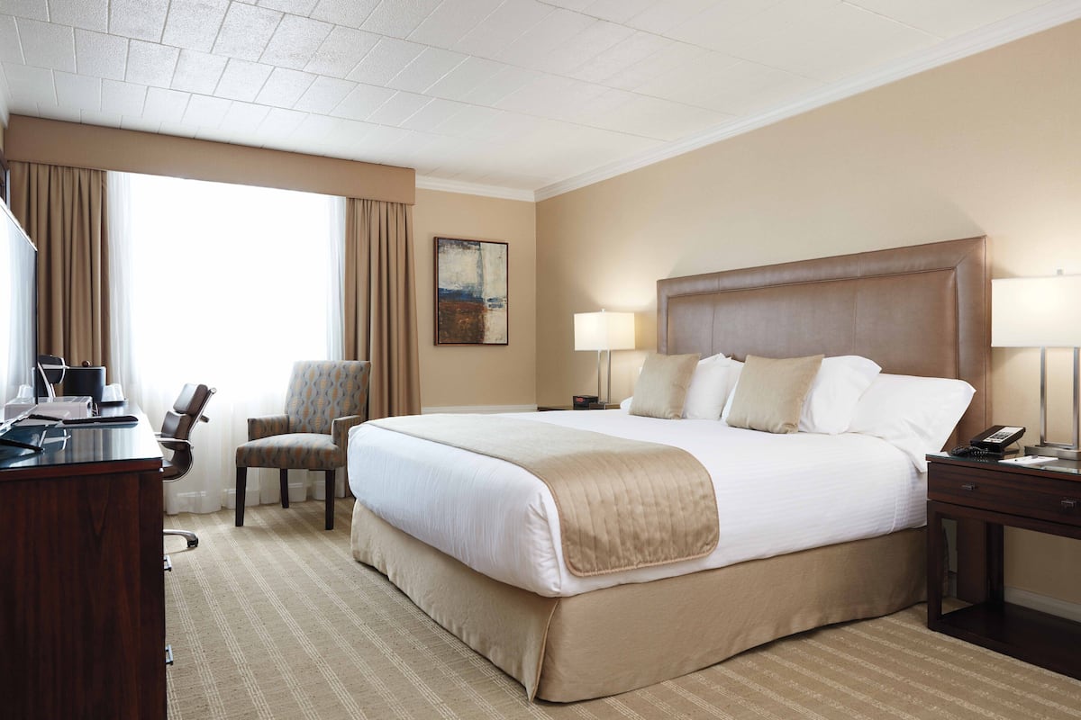 A hotel room with a large bed, two bedside tables, a desk, a chair, and a window with curtains.