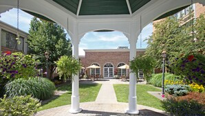 A covered garden area with a brick building in the background, a central pathway, and various plants and flowers. - Ethan Allen Hotel (Danbury)