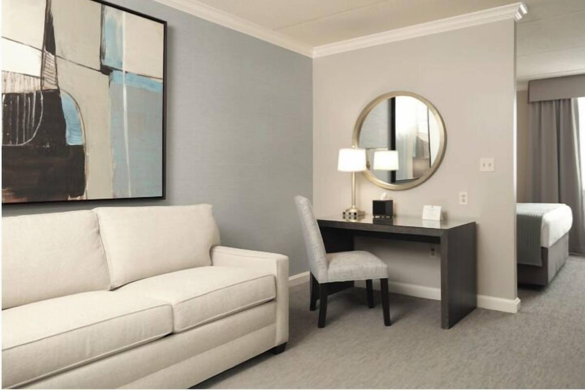 A hotel room with a white sofa, a desk with a chair, a round mirror, and a bed.