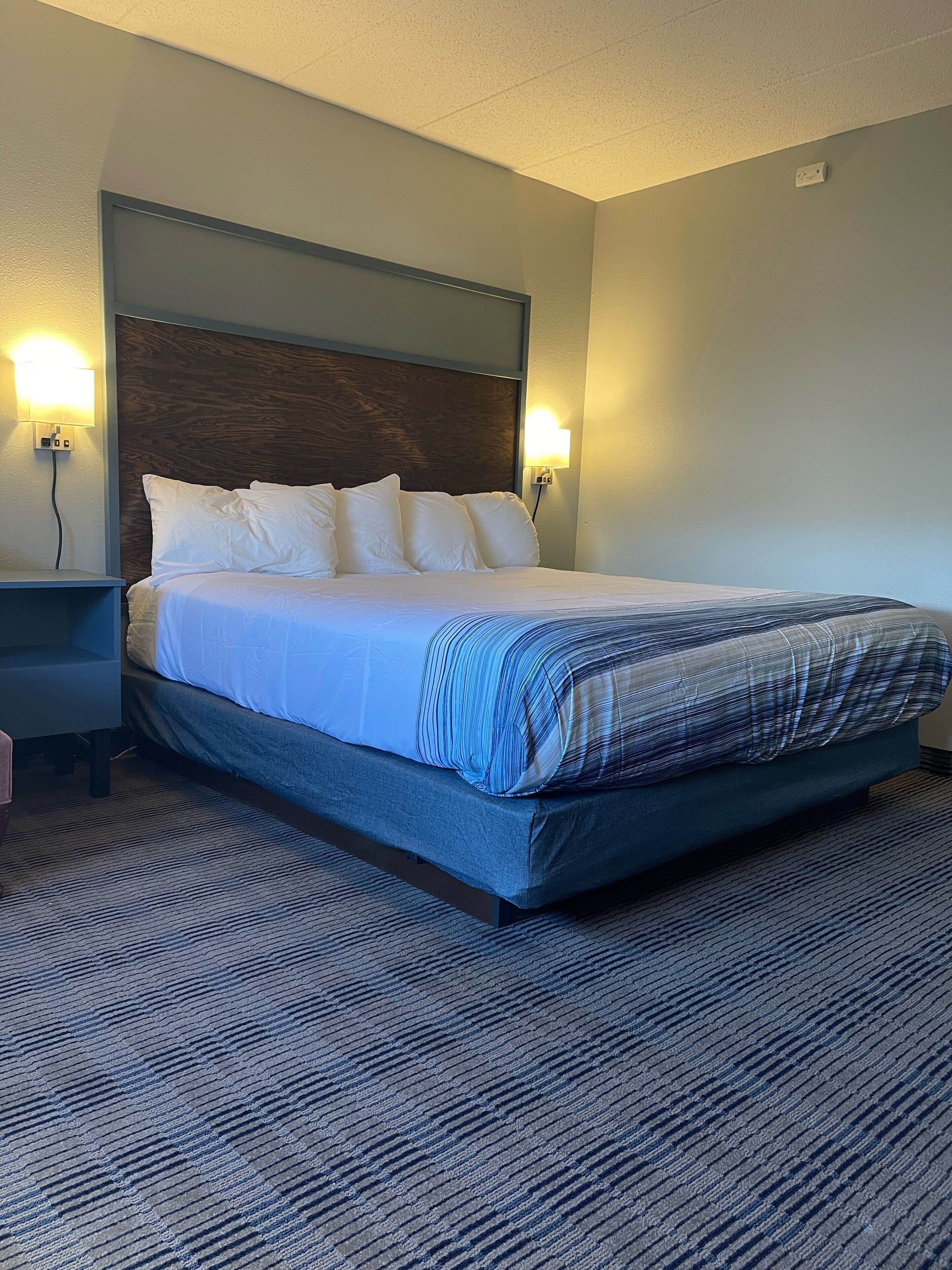 A neatly made bed with white and blue bedding, a dark headboard, and two wall-mounted lamps.