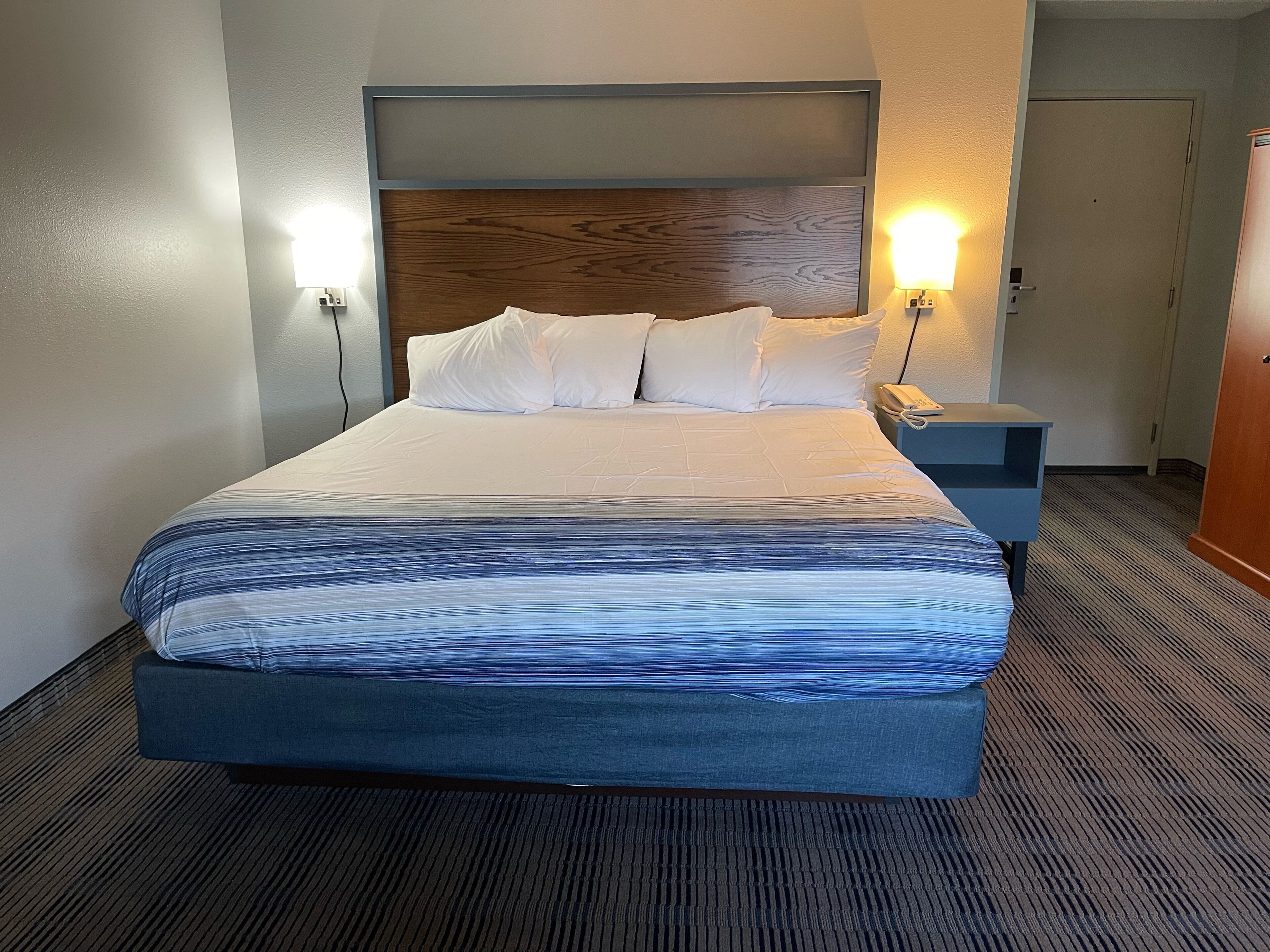 Een hotelkamer met een groot bed, twee bedlampen, een nachtkastje en een houten hoofdeinde.