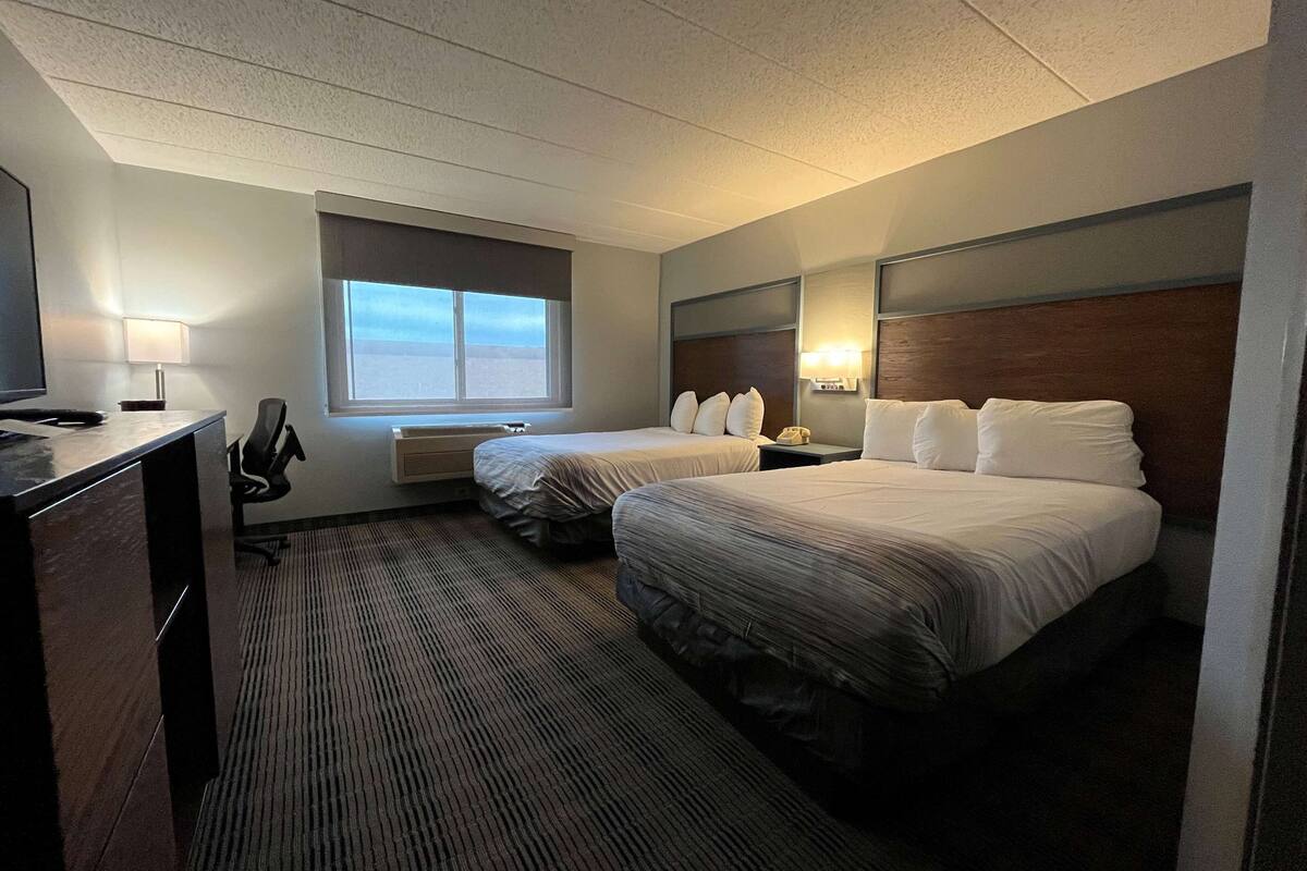 A hotel room with two beds, a desk with a chair, a window, and a TV.