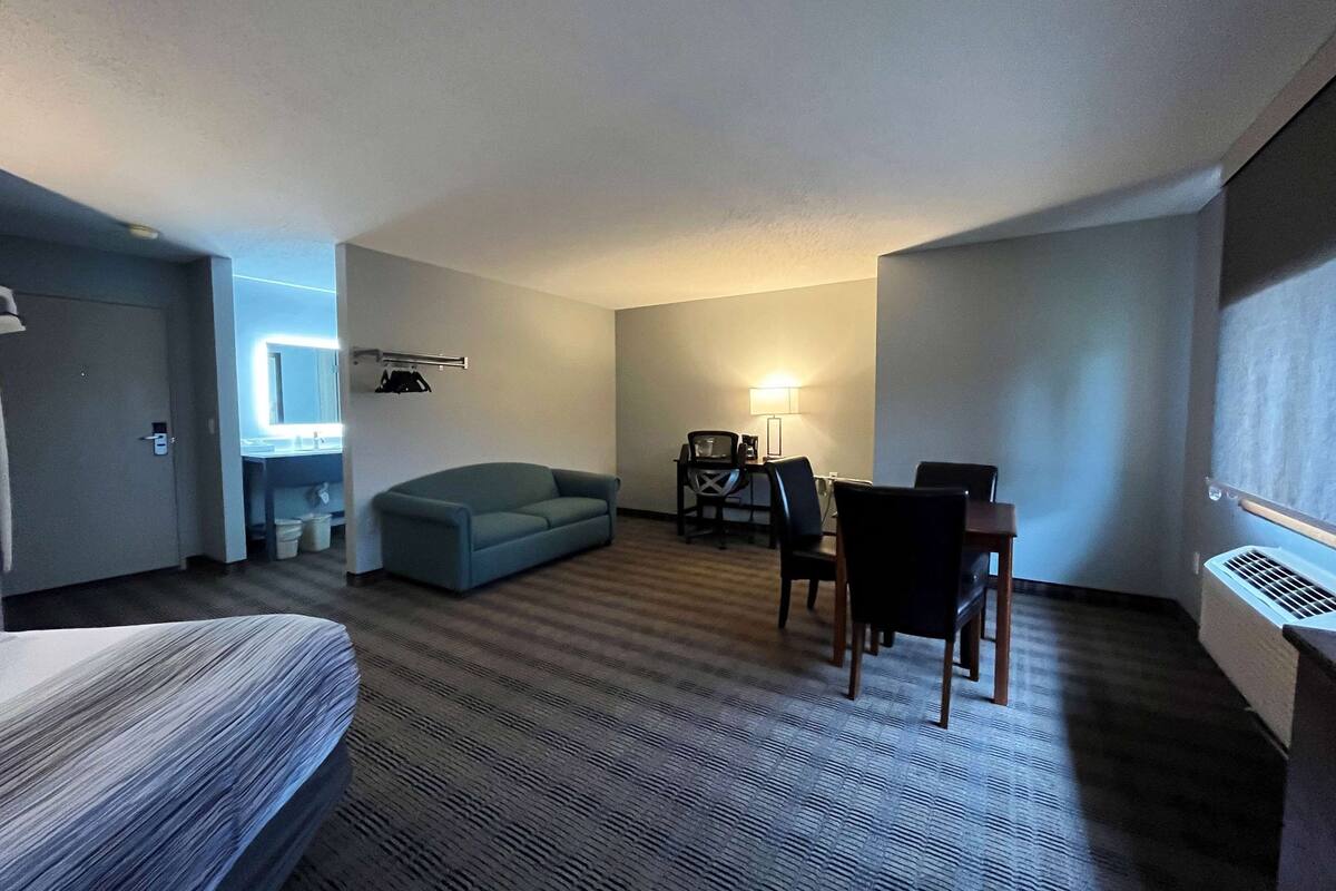 A hotel room with a bed, a sofa, a desk with chairs, a lamp, and a radiator.